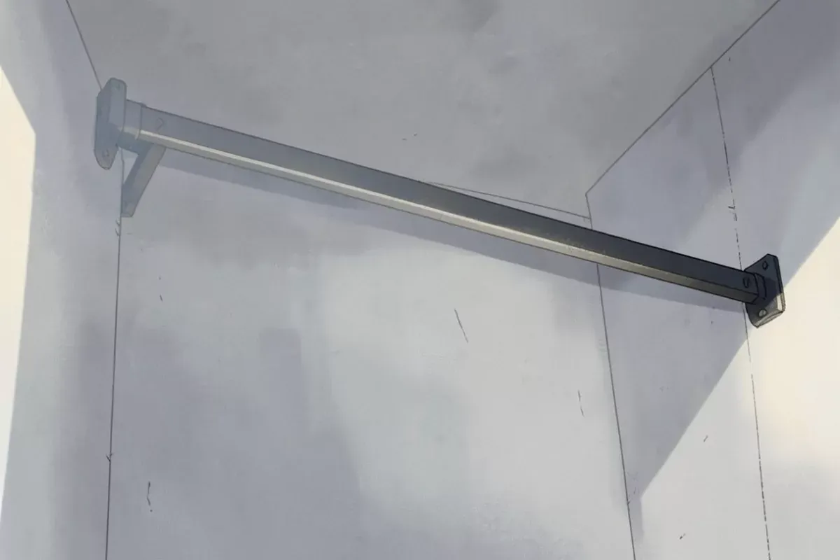 A steel pull up bar bolted to a plain wall in an empty room